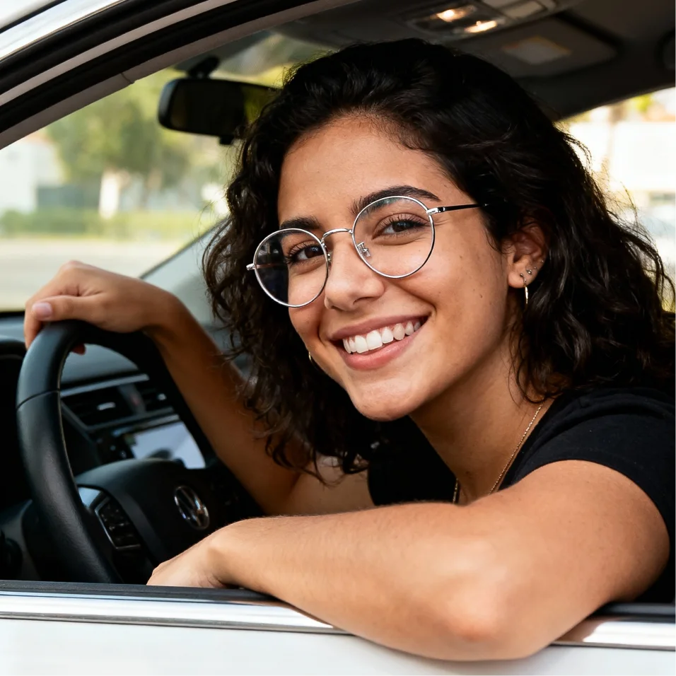 Mujer de pelo castaño en sentada en su coche asomándose por la ventanilla sonriendo